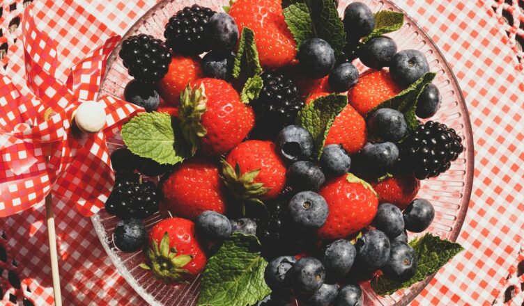 A vibrant mix of strawberries, blackberries, and blueberries with mint leaves in a glass bowl.