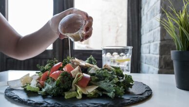 Hand pouring dressing over fresh salad with kale and tomatoes in a modern Dubai restaurant.