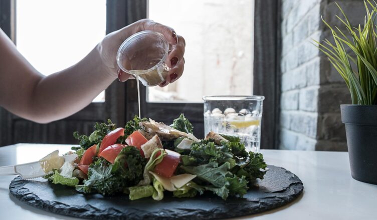 Hand pouring dressing over fresh salad with kale and tomatoes in a modern Dubai restaurant.