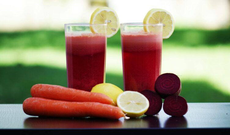 Colorful glasses of beetroot and carrot juice garnished with lemon slices, symbolizing health and freshness.