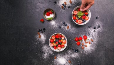 Fresh strawberries, blueberries, almonds in bowls on black table with hand arranging.