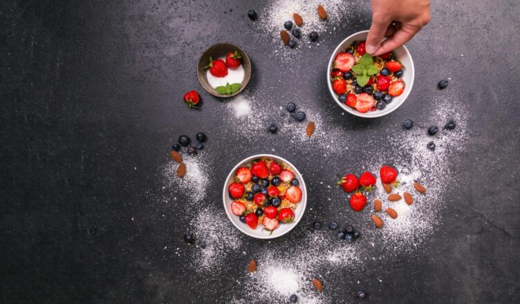 Fresh strawberries, blueberries, almonds in bowls on black table with hand arranging.