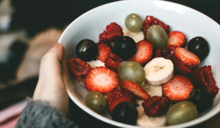 A close-up of a bowl filled with fresh strawberries, grapes, banana slices, and raspberries.